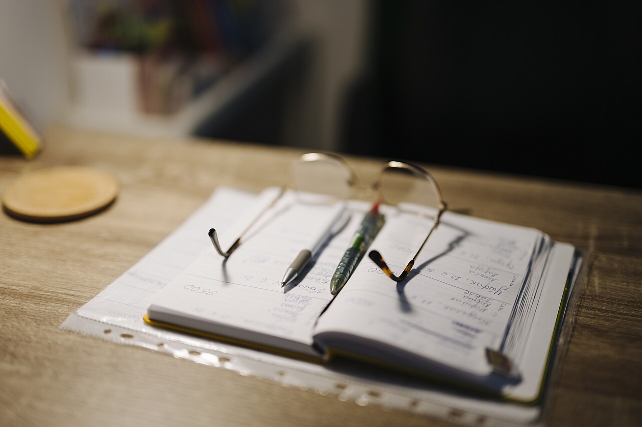 Notebook, pens and glasses arranged on a desk